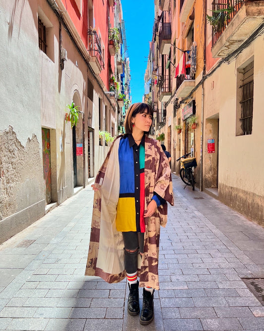 A person standing in a narrow street wearing a long, multicolored haori with a shika (deer) pattern.
